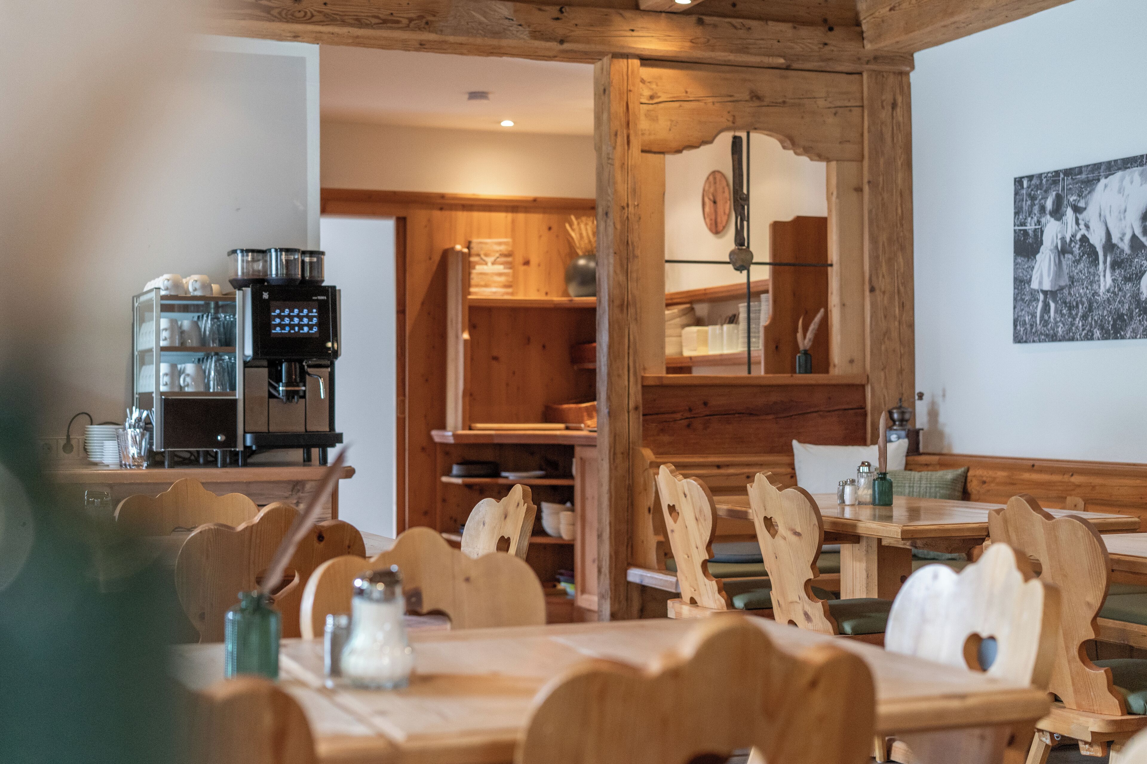 A rustic wooden interior with a coffee machine, wooden chairs, and a dining table.