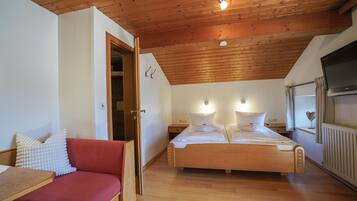 Une chambre avec un plafond en bois, un lit avec une literie blanche, un canapé rouge et un téléviseur fixé au mur.