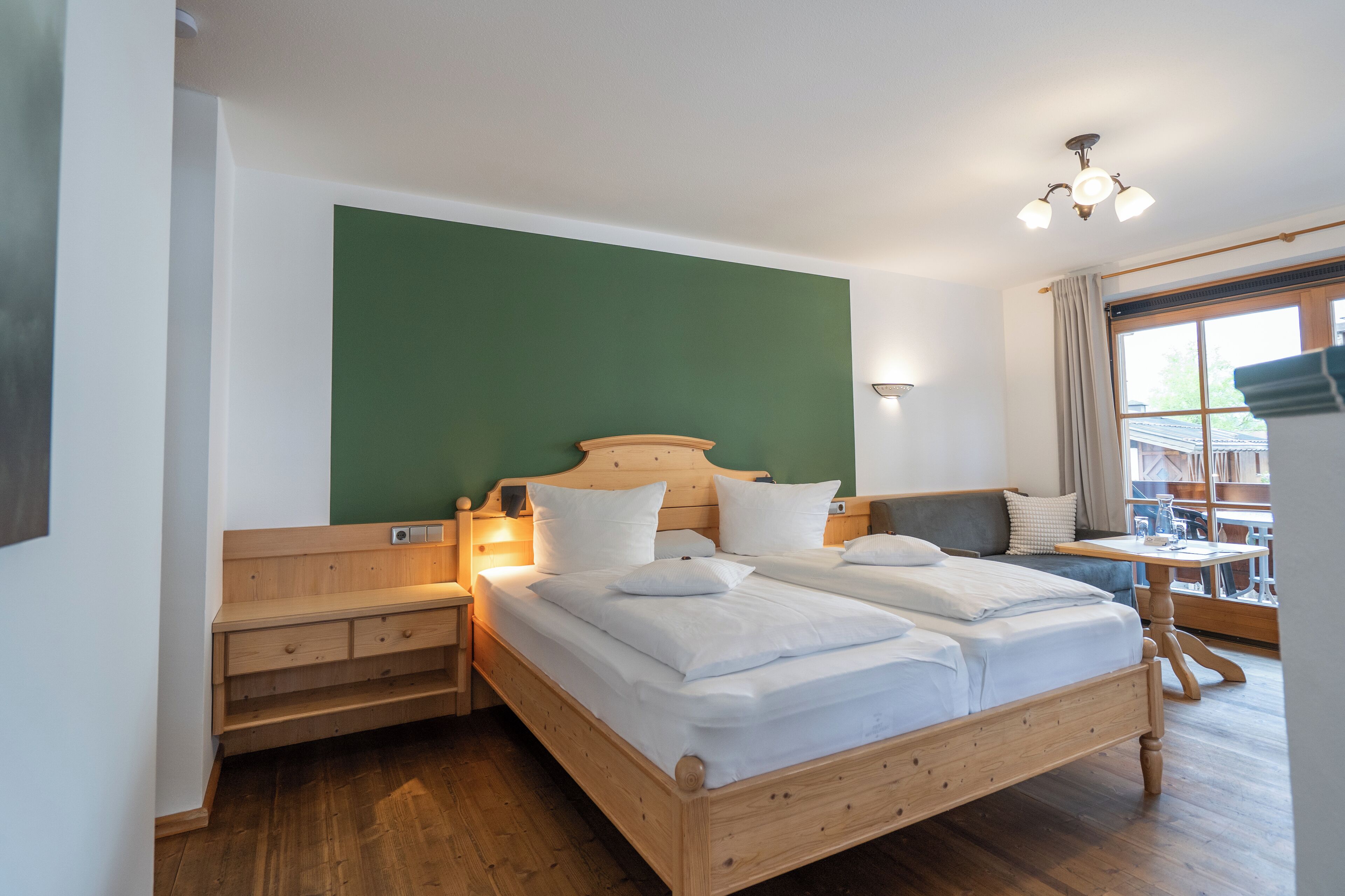 Cama doble con cabecera y piecera de madera, mesita de noche y pared verde decorativa.