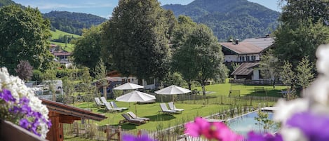 A pool area with lounge chairs and umbrellas, surrounded by lush greenery and mountains in the background.