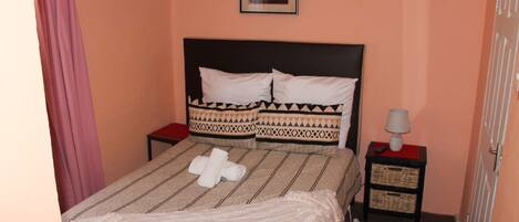 Una cama bien hecha con una colcha a rayas y almohadas, un cuadro enmarcado en la pared y una mesita de noche con una lámpara.