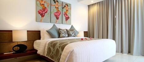 A hotel room with a large bed, a nightstand, a lamp, and three paintings on the wall.