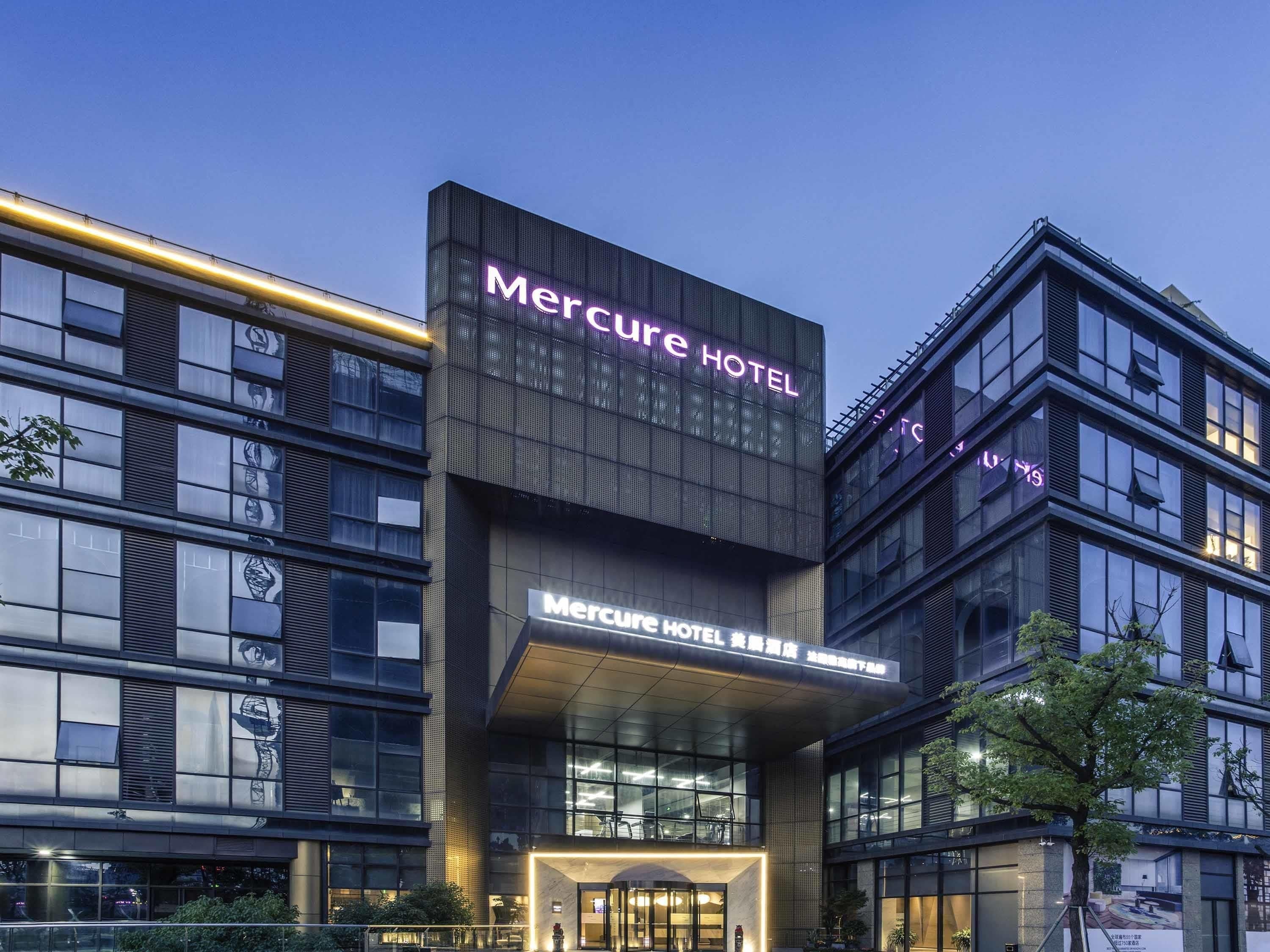 A modern hotel building with a prominent sign reading 'Mercure HOTEL' and another sign in a different language below it.