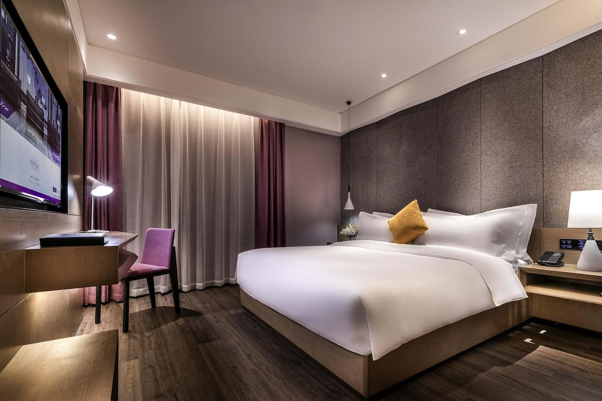 A modern hotel room with a bed, desk, chair, and a television displaying a room service menu.