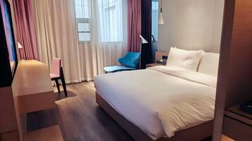 Quarto de hotel moderno com uma cama grande, uma escrivaninha, uma cadeira e uma luminária de mesa.