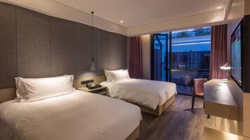 A modern hotel room with two beds, a desk, and a view of the outdoors.