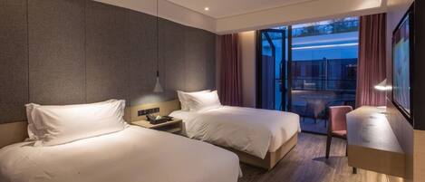 A modern hotel room with two beds, a desk, and a view of the outdoors.