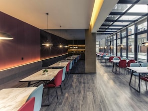 A modern dining area with long tables and chairs, a central column, and large windows allowing natural light. - Mercure Suzhou Downtown (Suzhou)