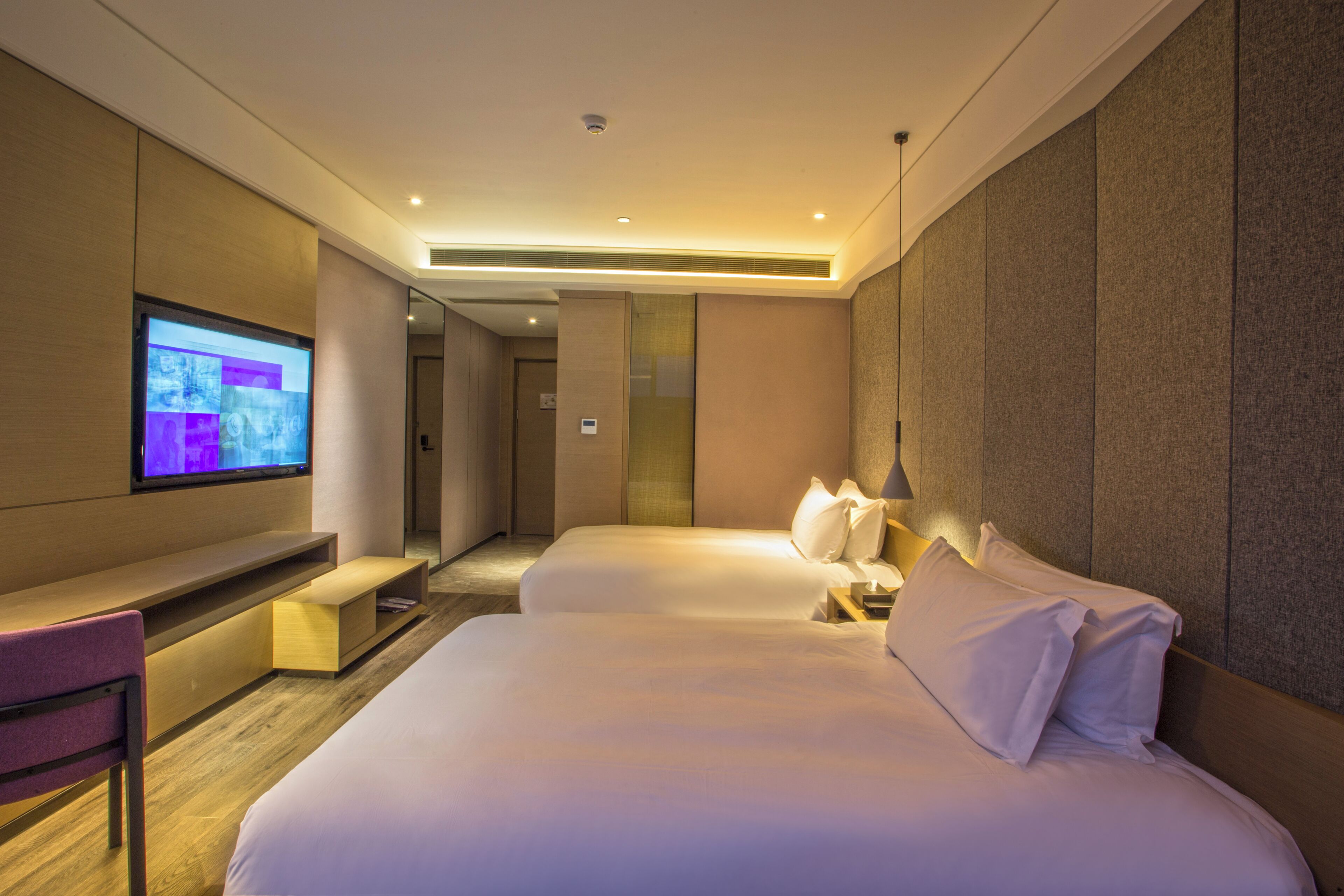 A hotel room with two beds, a TV, a desk, and a chair.