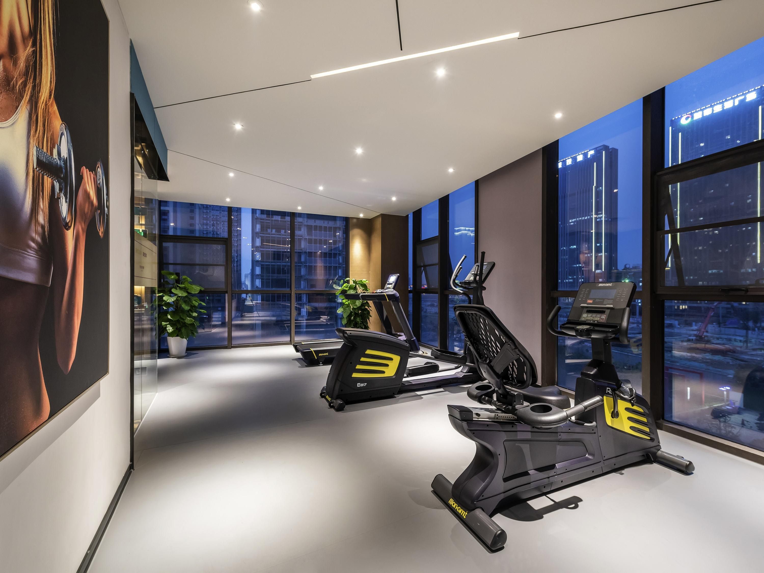 Un gimnasio moderno con equipo de ejercicio, ventanas amplias y vista a la ciudad.