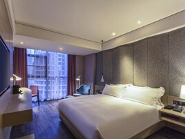 A hotel room with a large bed, a desk, a chair, and a TV.