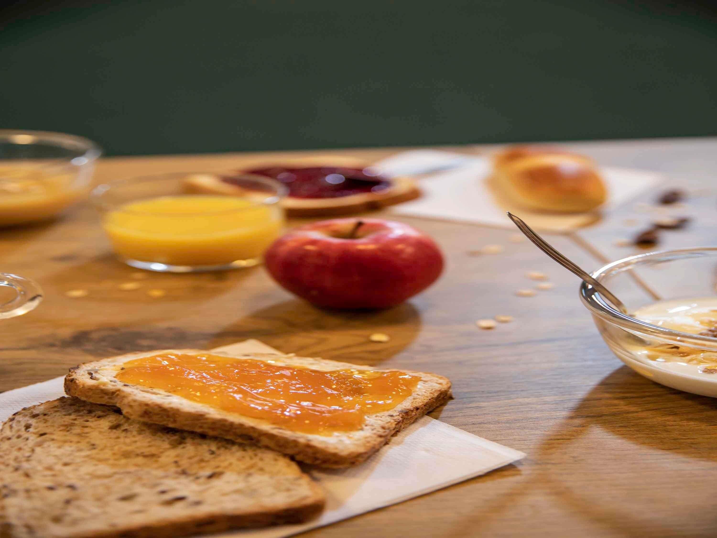 A wooden table with breakfast items including toast, apple, orange juice, and a bowl of cereal.