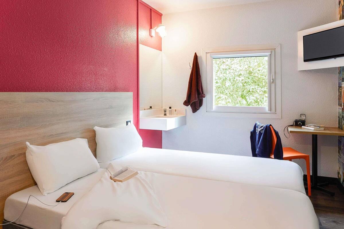 Quarto de hotel com uma cama, mesa de cabeceira, televisão, janela e pia.