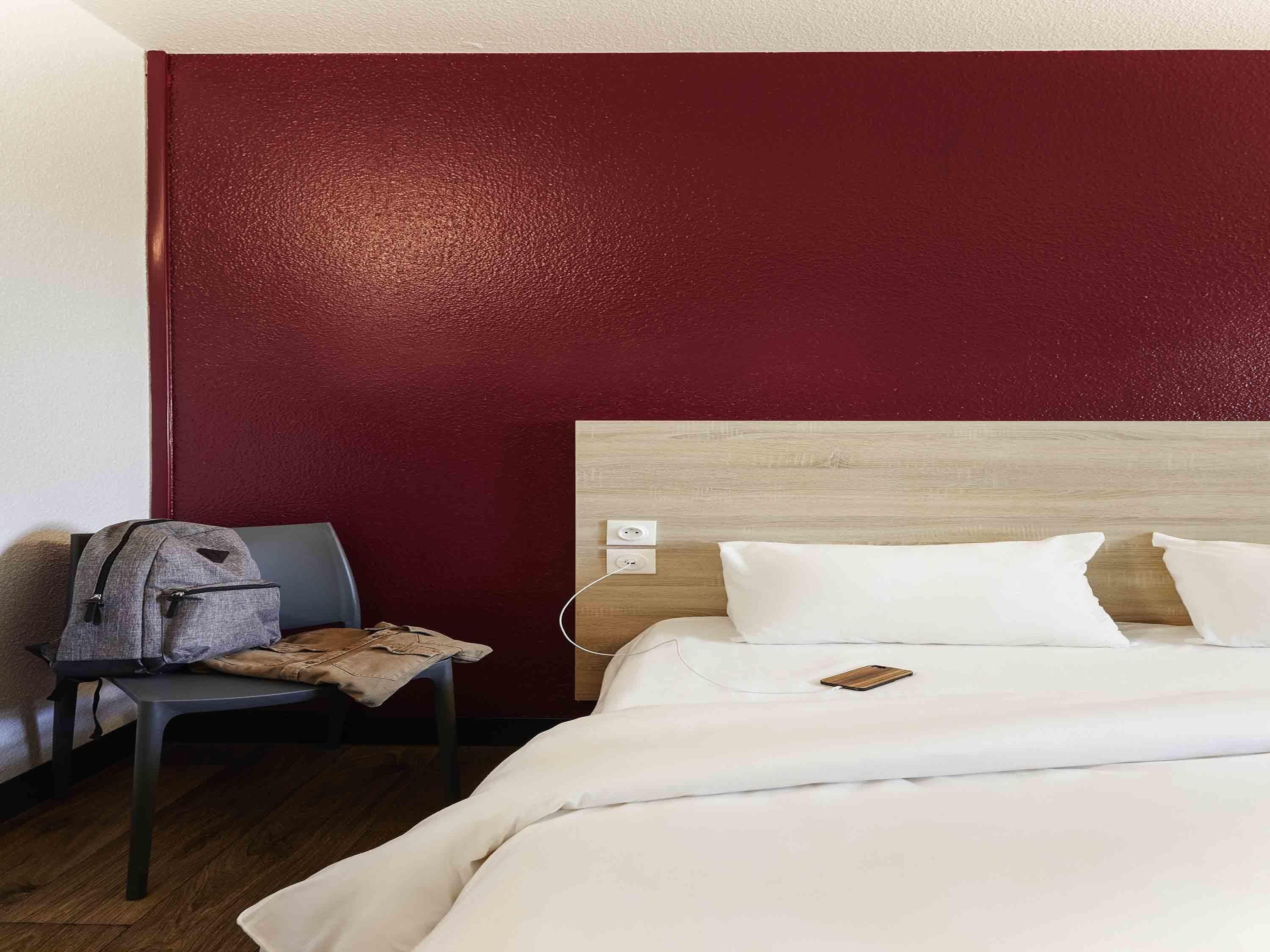 Une chambre d’hôtel avec un lit, une chaise, un sac à dos et une tête de lit en bois.