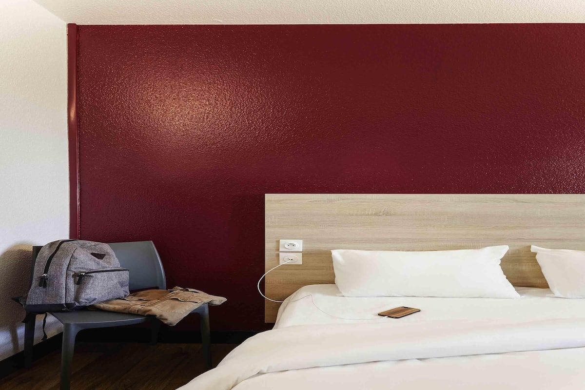 Une chambre dâhĂŽtel avec un lit, une chaise, un sac Ă dos et une tĂȘte de lit en bois.