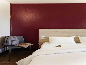 A hotel room with a bed, a chair, a backpack, and a wooden headboard. - hotelF1 Fréjus Roquebrune-sur-Argens (Hôtel rénové) (Roquebrune-sur-Argens)
