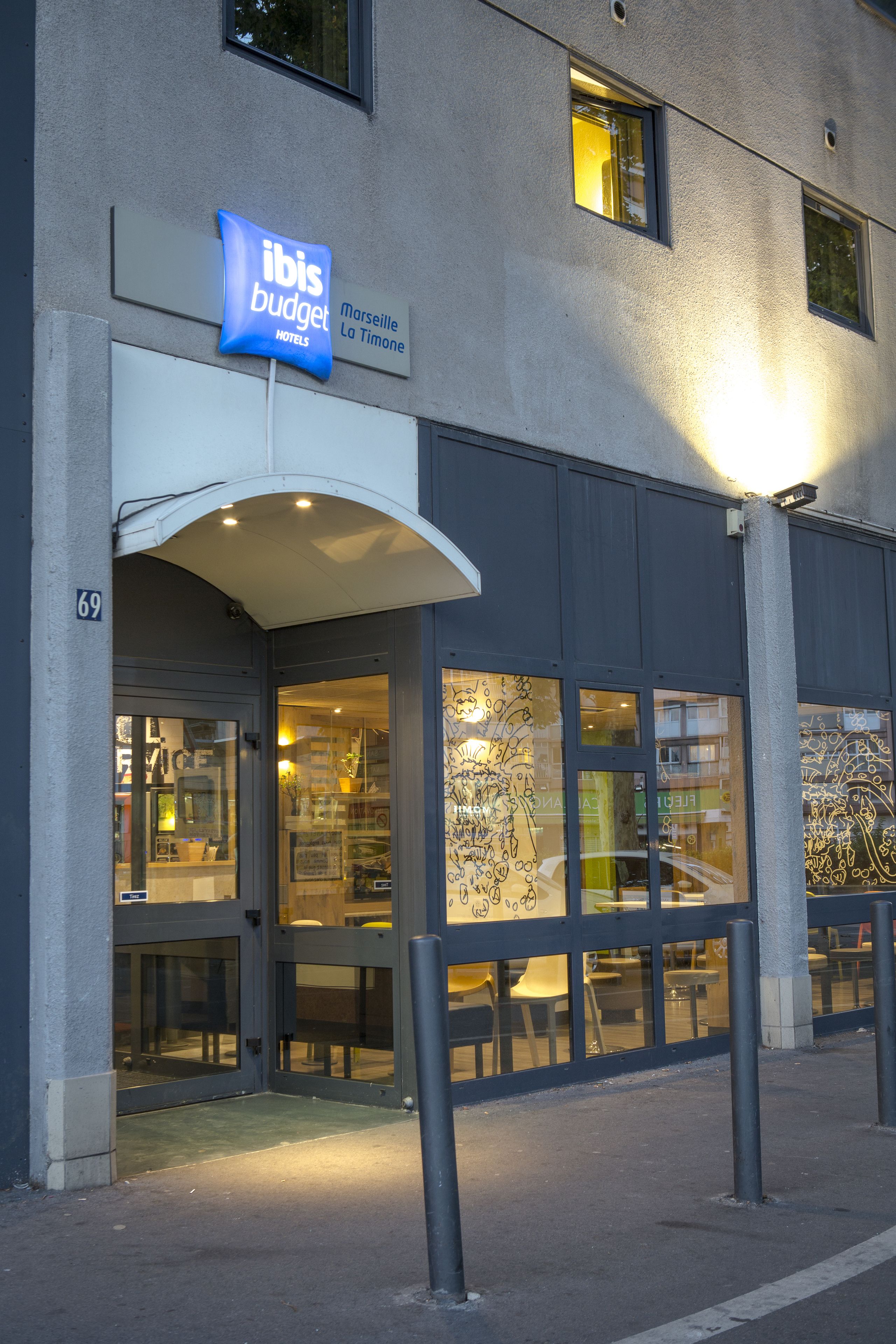 A building with a sign for ibis budget hotels, large windows, and a covered entrance.