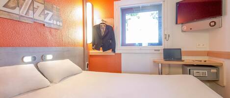 A hotel room with a bed, a TV, a desk with a laptop, a safe, and a window with a view.