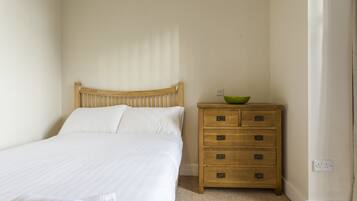 A neatly made bed with white linens, a wooden headboard, and a wooden dresser with drawers.