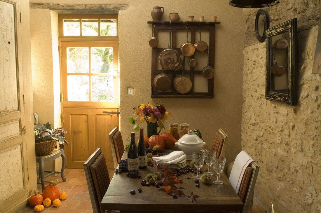 Uma área de refeições com uma mesa de madeira posta para uma refeição, cercada por cadeiras. Uma janela com vista para o verde é visível, e uma prateleira com vasos suspensa acima da mesa.