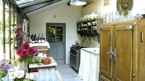 A kitchen with a wooden cabinet, a dining table with flowers, and a wine rack. - Le Moulin Bregeon (Noyant-Villages)
