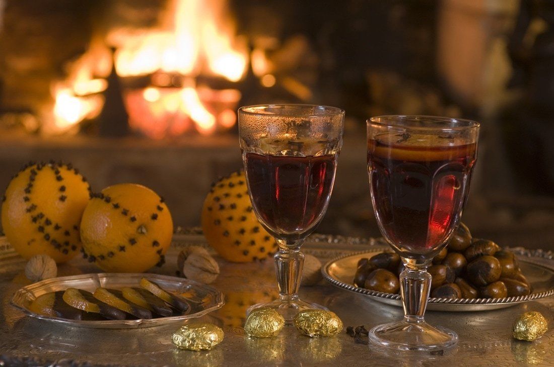 Two glasses of red wine, a plate of nuts, and a plate of olives, with a fire in the background.