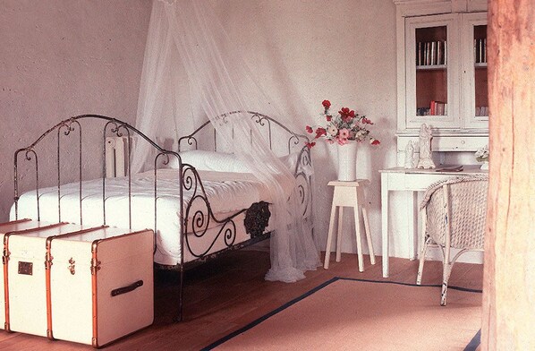 A bedroom with a metal bed frame, a bedside table with a vase of flowers, a white cabinet, and a suitcase on the floor. - Le Moulin Bregeon (Noyant-Villages)