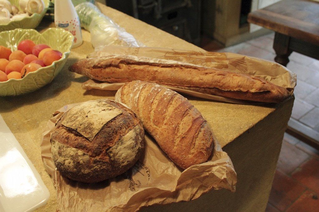 A table with three loaves of bread and a bowl of fruit.