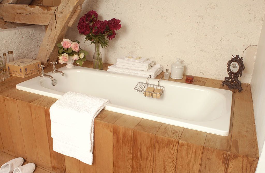 A bathroom with a wooden vanity, a white bathtub, a mirror, and a vase with flowers.
