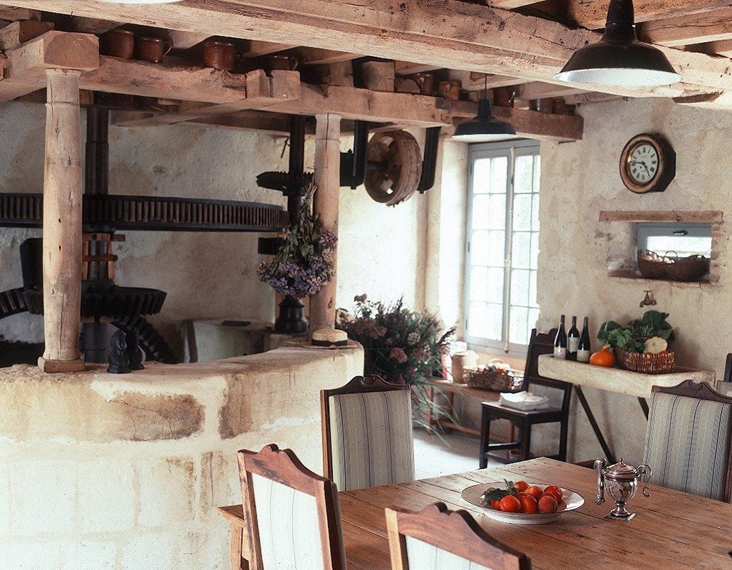 Une cuisine rustique avec des poutres en bois, une table à manger avec des chaises et une horloge au mur.