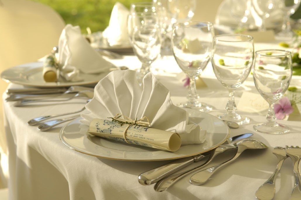 Een tafel gedekt voor een formeel evenement, met witte tafellinnen, bestek en glazen.