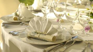 Een tafel gedekt voor een formeel evenement, met witte tafellinnen, bestek en glazen.