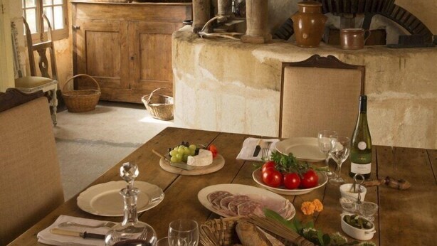 A rustic dining room with a wooden table set for a meal, featuring bread, tomatoes, and a bottle of wine. - Le Moulin Bregeon (Noyant-Villages)