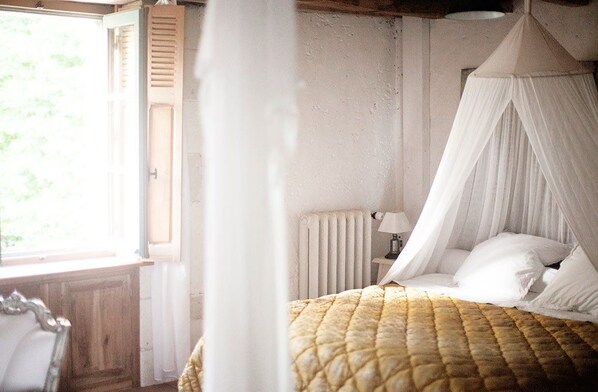 A bedroom with a bed under a canopy, a window, and a radiator. - Le Moulin Bregeon (Noyant-Villages)