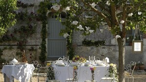 An outdoor dining setup with white tablecloths, metal chairs, and a rustic stone wall in the background. - Le Moulin Bregeon (Noyant-Villages)