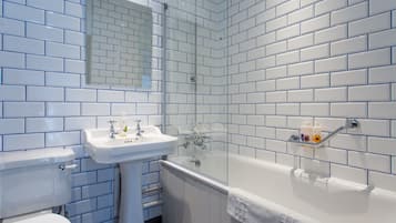 Un baño con azulejos blancos tipo metro, un lavamanos blanco, una bañera y un inodoro.