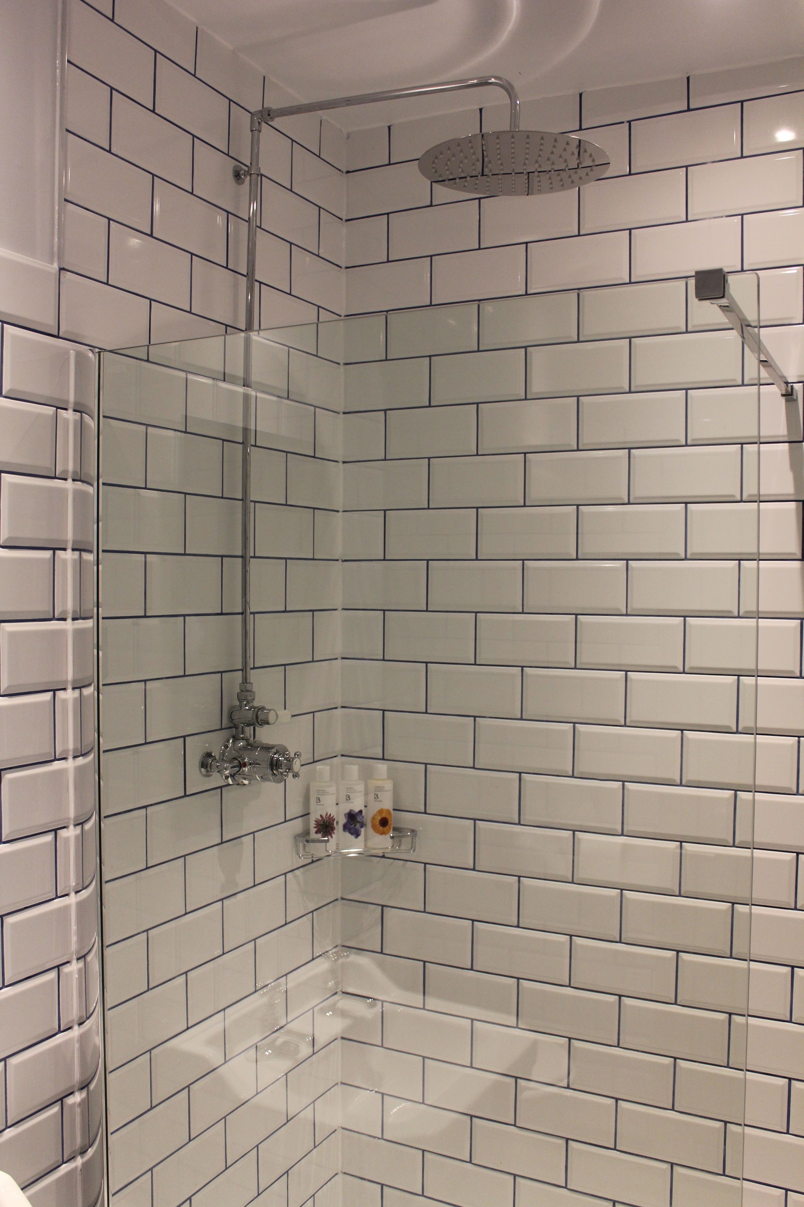Eine Dusche mit weißen Fliesen im U-Bahn-Stil und einer Glasabtrennung.