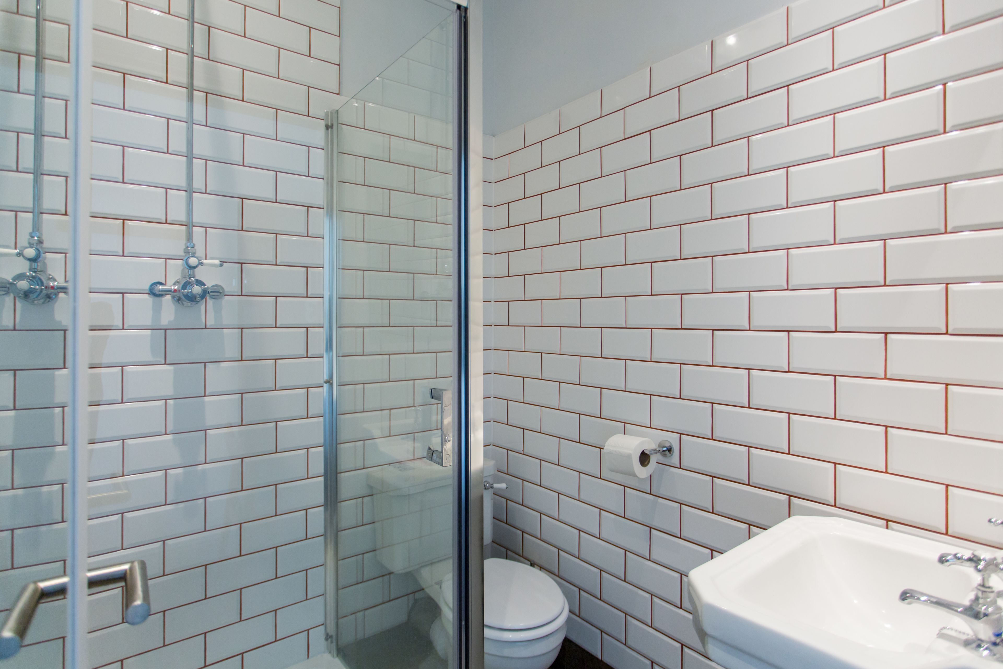 A bathroom with white subway tiles, a glass shower enclosure, a white toilet, and a sink with a mirror.
