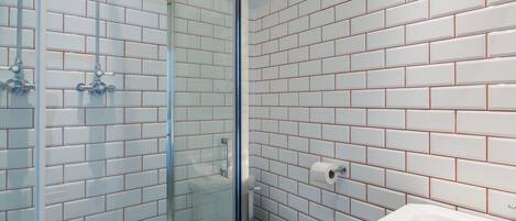 A bathroom with white subway tiles, a glass shower enclosure, a white toilet, and a sink with a mirror.