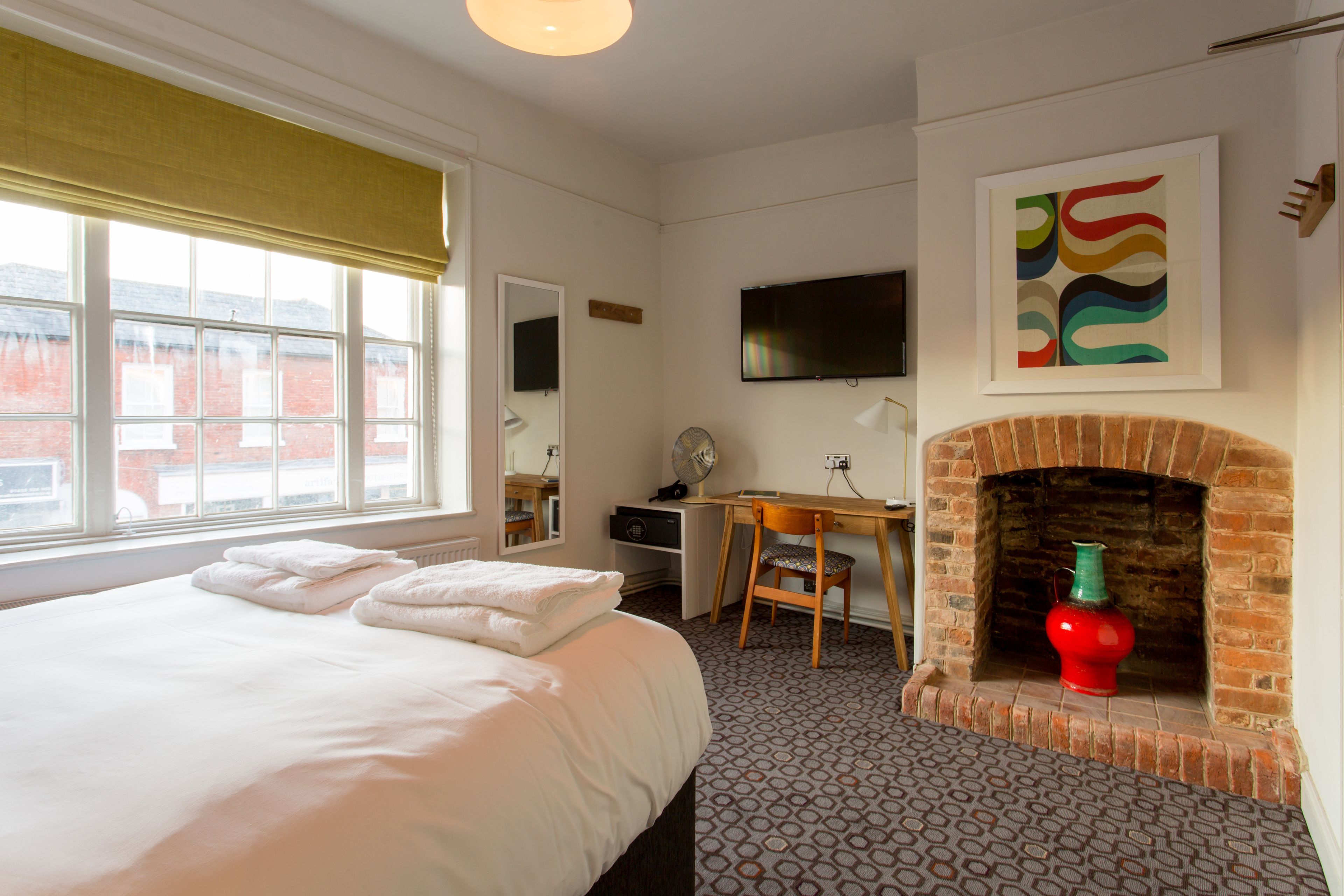 Hotelkamer met een bed, bureau, televisie, open haard en een raam met uitzicht op gebouwen.