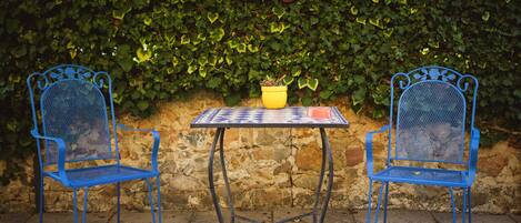 Two blue metal chairs and a small table with a potted plant in front of a stone wall covered with green ivy.