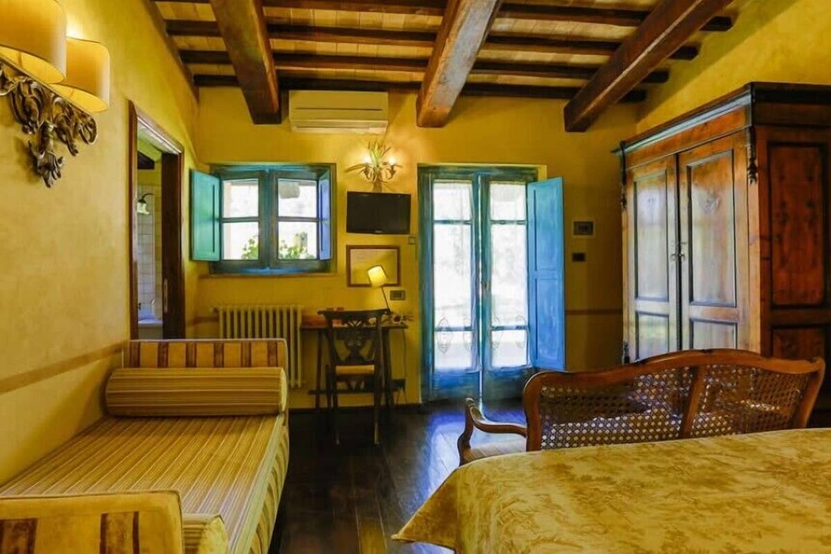 A room with a wooden ceiling, a bed, a table with chairs, and a window with shutters.