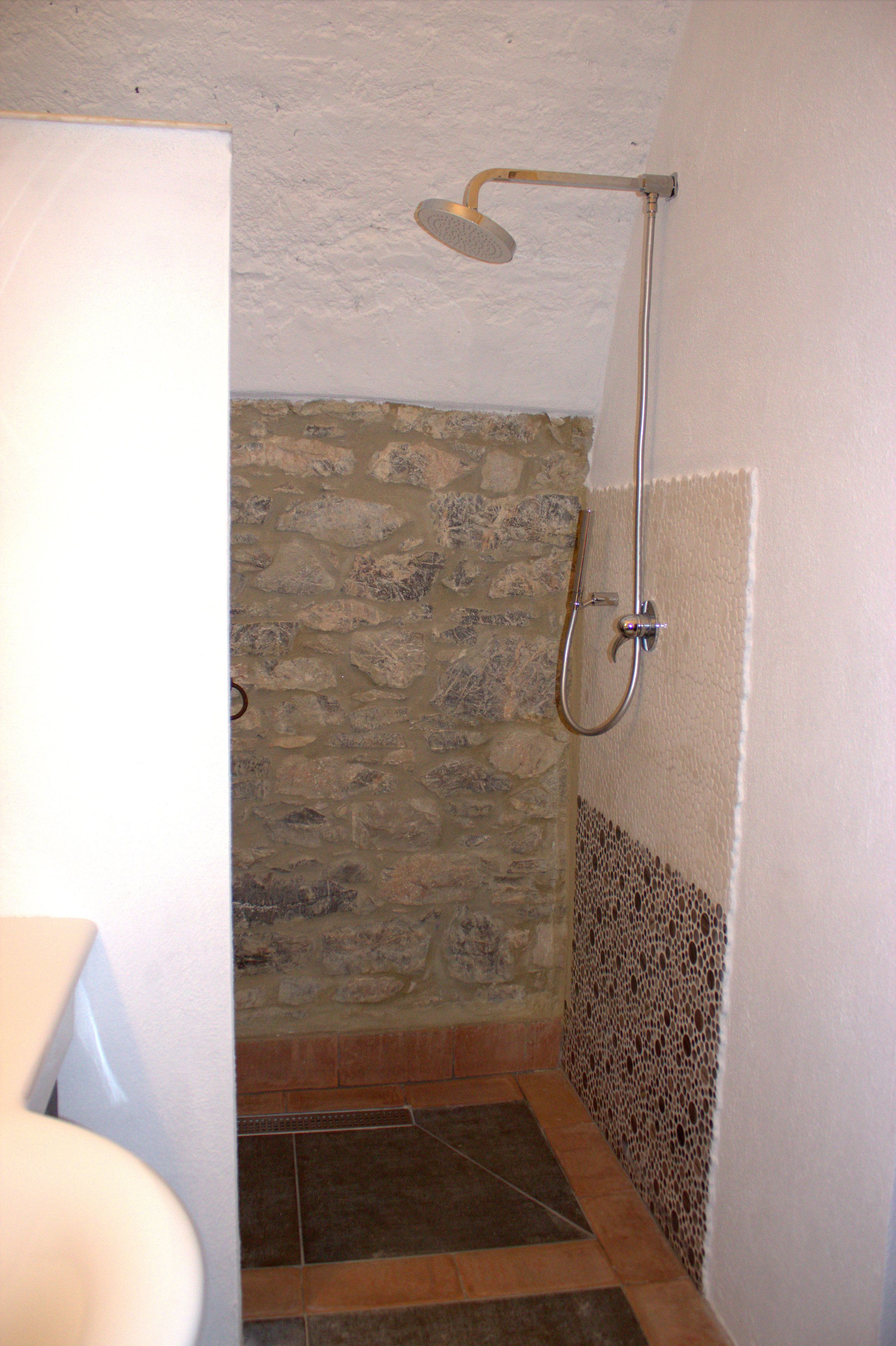 A shower with a stone wall, a tiled floor, and a white wall with a decorative border.