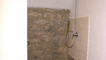 A shower with a stone wall, a tiled floor, and a white wall with a decorative border.