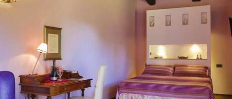 A bedroom with a bed, a desk, a chair, and a hanging shelf with framed pictures.