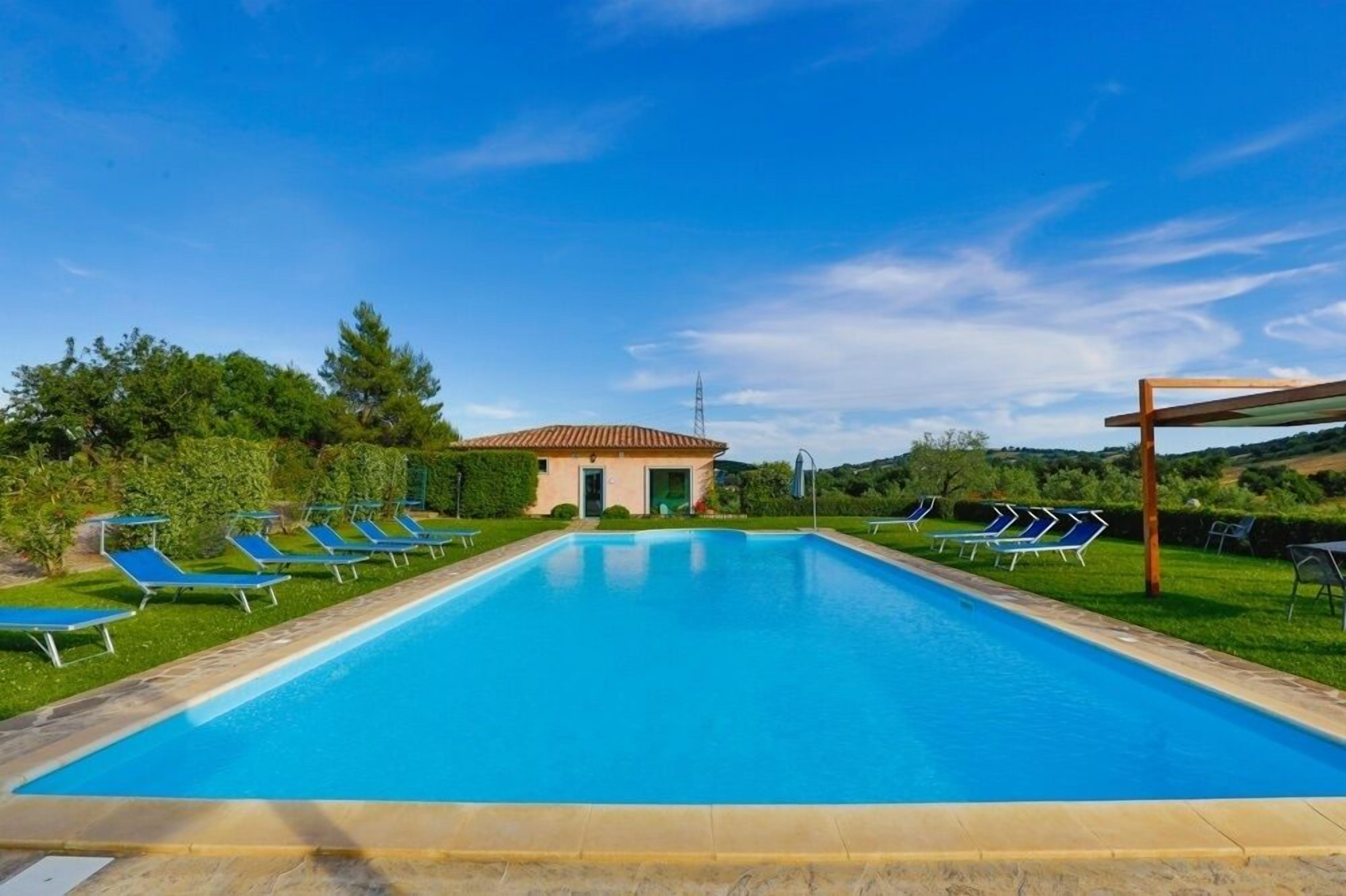 A swimming pool with lounge chairs, a small building, and a clear sky.