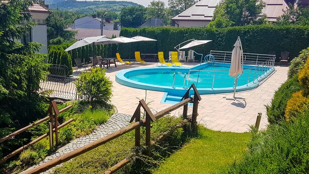 A swimming pool surrounded by yellow lounge chairs and umbrellas, with a wooden fence and greenery. - JANDA Resort & Conference (Mszana Dolna)