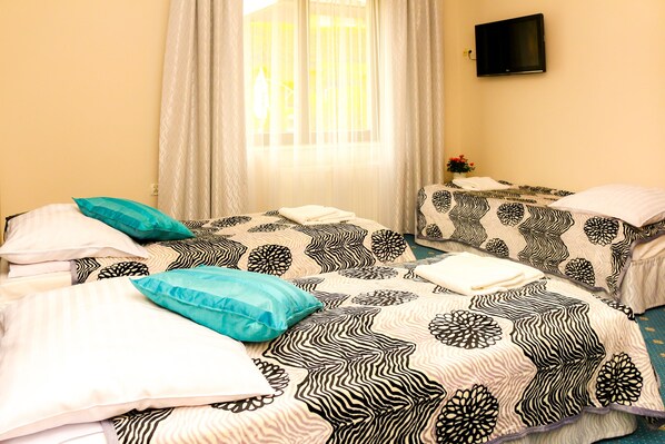 Une chambre d’hôtel avec deux lits, chacun agrémenté de draps à motifs, un téléviseur fixé au mur et une fenêtre avec des rideaux.