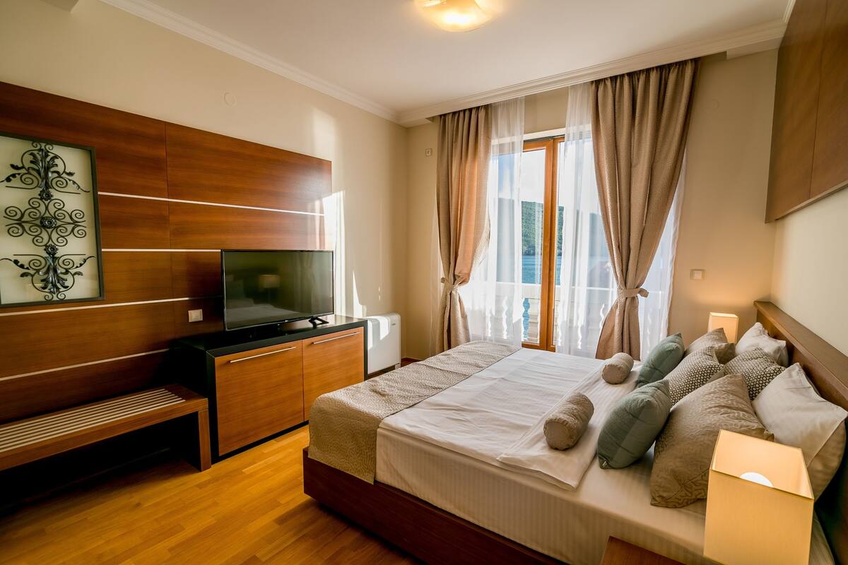 A bedroom with a bed, a TV, a wooden cabinet, and a window with curtains.