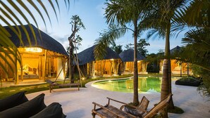 Un resort con villas de techo de paja, una piscina y zonas de estar al aire libre.